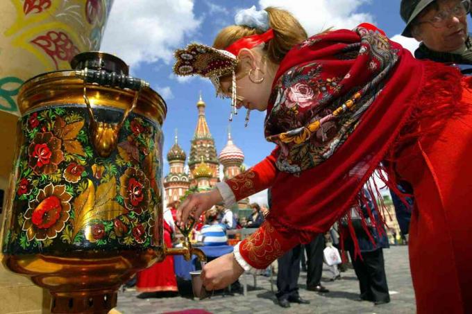 Ruska deklica, ki nosi tradicionalna oblačila, izliva vodo iz samovarja