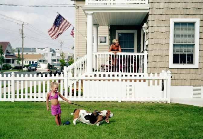 Niña con perro delante de su casa. Bandera americana ondeando