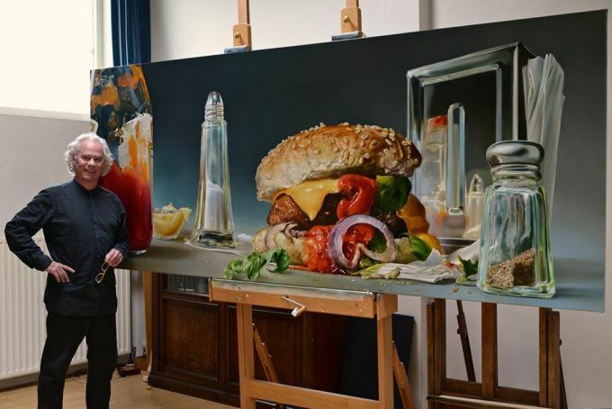 Človek stoji s preveliko podobo hamburgerja in stresalnikov soli in popra.