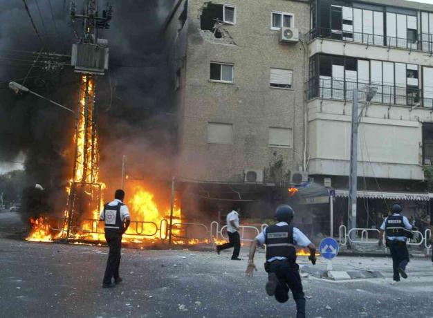 Izraelski policisti se odpravijo na kraj gorečega pilona z električno energijo in so poškodovali stavbe v trenutku, ko je odbojka raket Hezbollah 13. julija 2006 udarila v severnem mestu Nahariya v Izraelu.